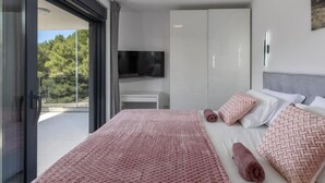 Ein modernes Schlafzimmer mit Bett, Fernseher und Balkon mit Blick auf Bäume.