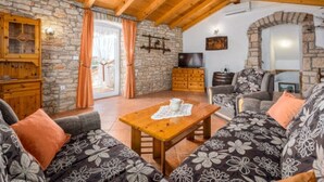Una sala de estar acogedora con una pared de piedra, vigas de madera en el techo, un conjunto de sofás, una mesa de centro de madera y un televisor.
