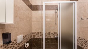 A shower with a glass door, a towel rack, and a toilet paper holder on the wall.