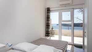 A bedroom with a bed, a nightstand, a desk, and a view of a balcony with a table and chairs.