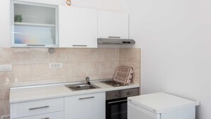 Eine kompakte Küche mit weißen Schränken, einem eingebauten Backofen, einem Geschirrspüler und einem kleinen Kühlschrank.