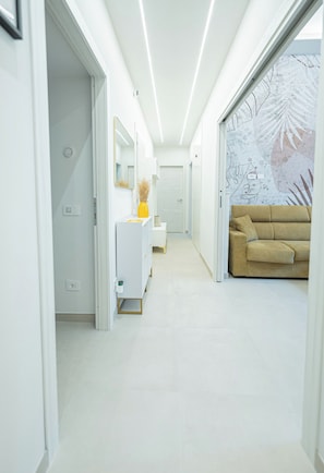 A modern hallway with a white floor, a beige sofa, a white cabinet with a mirror, and a wall with a leaf pattern.