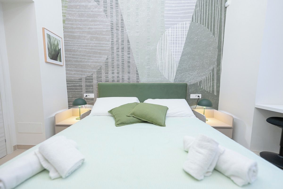 A hotel room with a bed, pillows, two bedside tables with lamps, a wall art piece, and a framed picture on the wall.