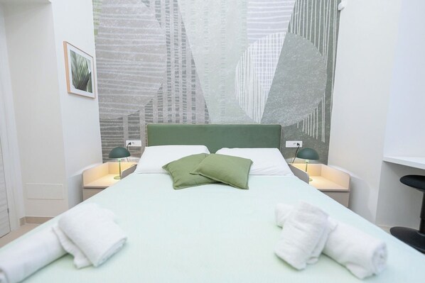 A hotel room with a bed, pillows, two bedside tables with lamps, a wall art piece, and a framed picture on the wall.