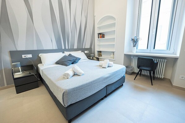 A modern bedroom with a bed, bedside tables, a chair, a radiator, and a window.