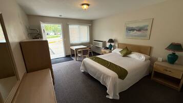 Een hotelkamer met een bed, nachtkastje, lamp, stoel, bureau en een schilderij aan de muur.