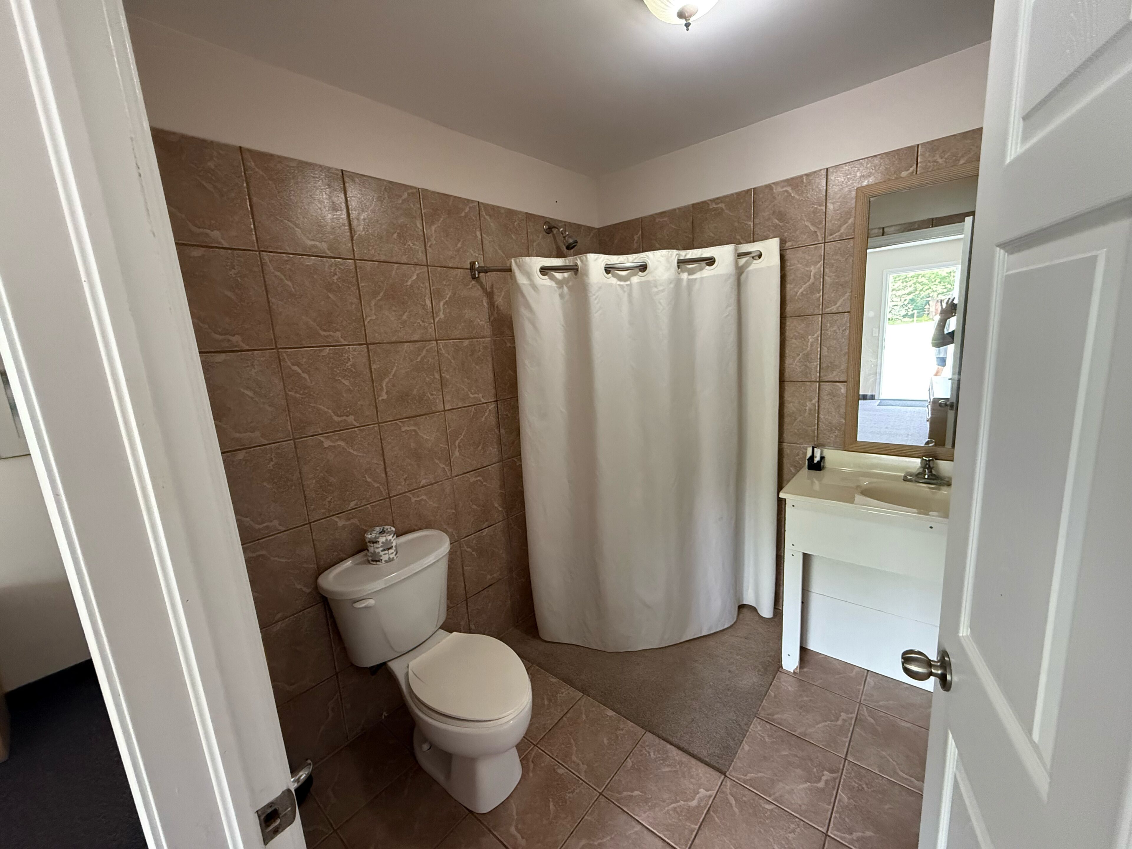 A bathroom with a toilet, shower curtain, and sink.