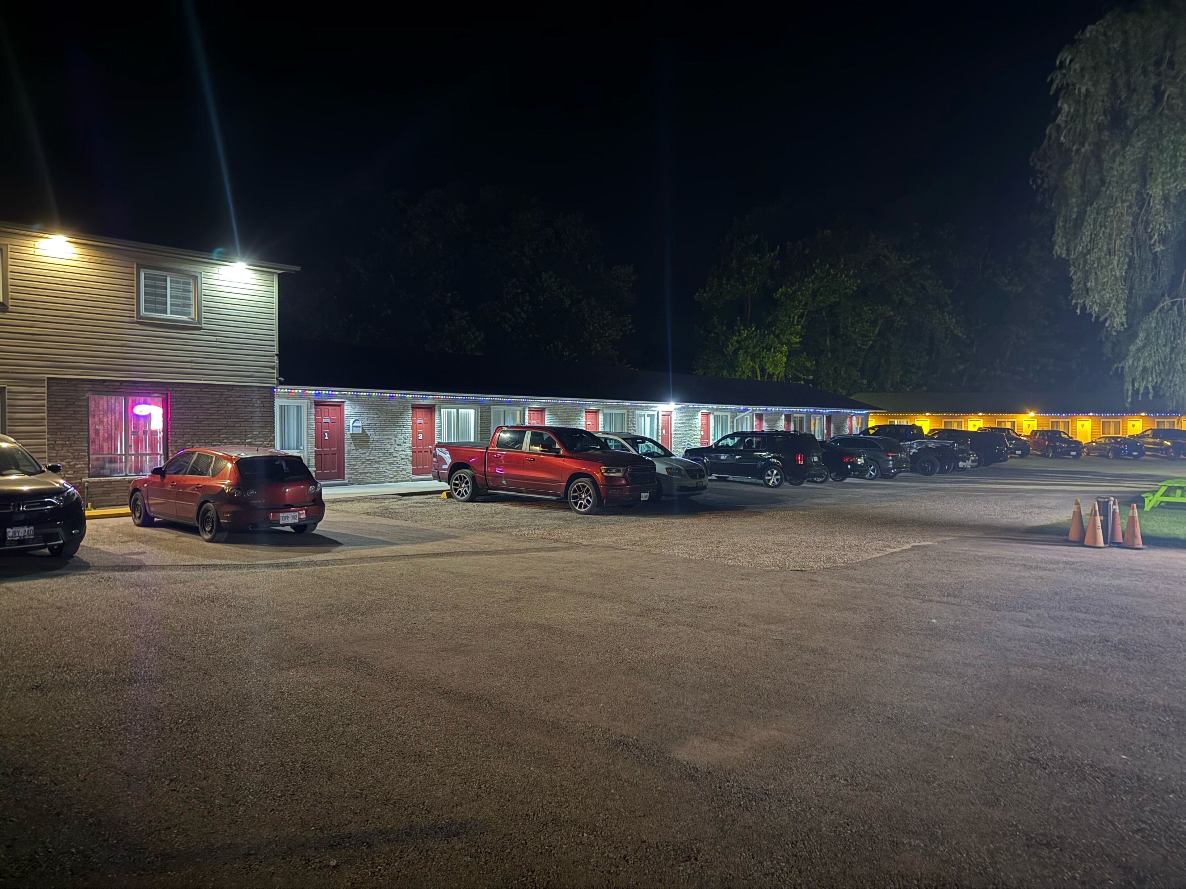 Un motel con varias habitaciones, un estacionamiento y una fila de coches aparcados.