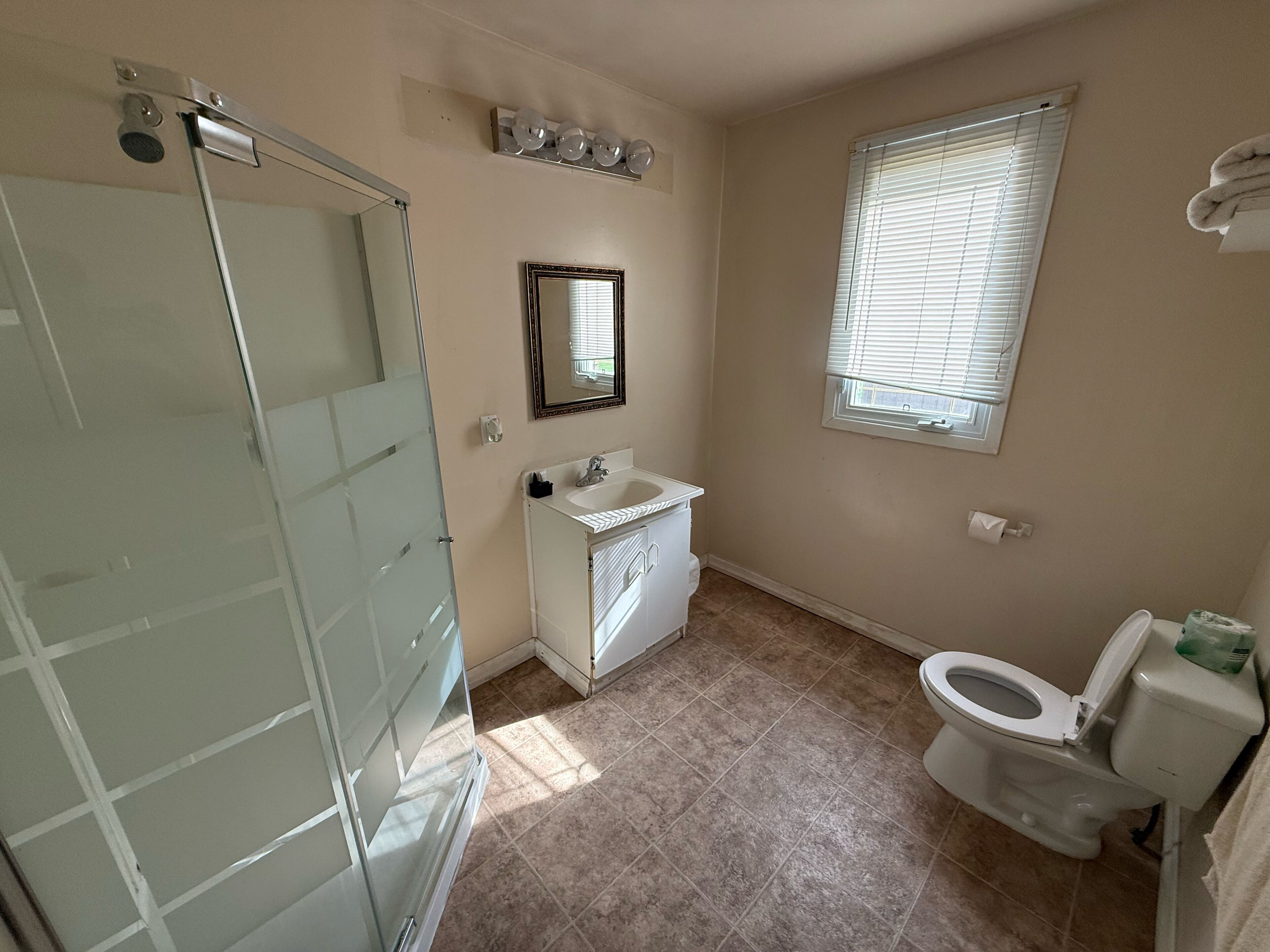 A bathroom with a glass shower door, a sink with a mirror, and a toilet.