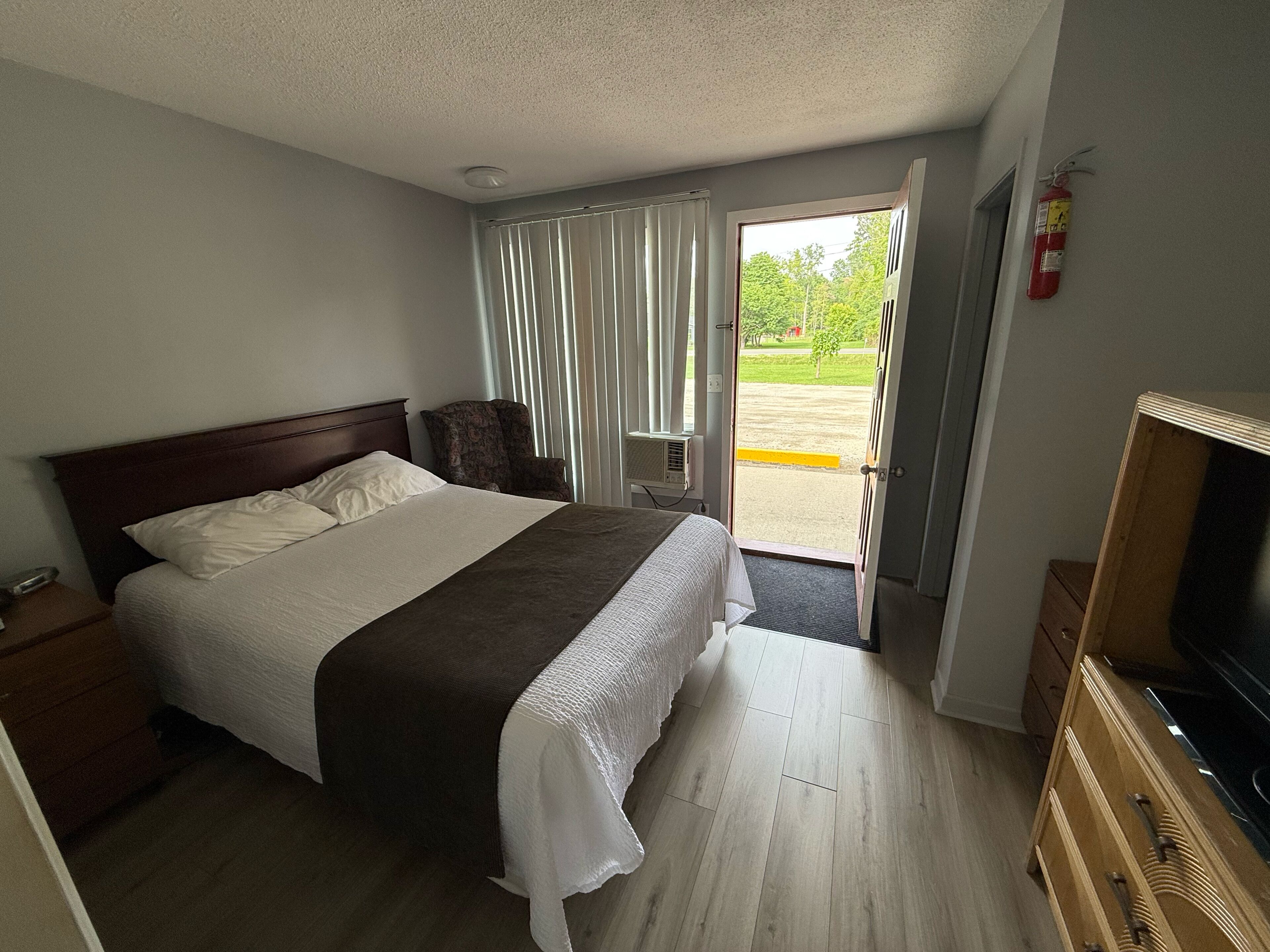 A hotel room with a bed, a television, a wooden dresser, and a window with curtains.
