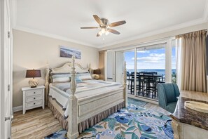 A bedroom with a four-poster bed, a ceiling fan, a view of the ocean, and a balcony with outdoor furniture.