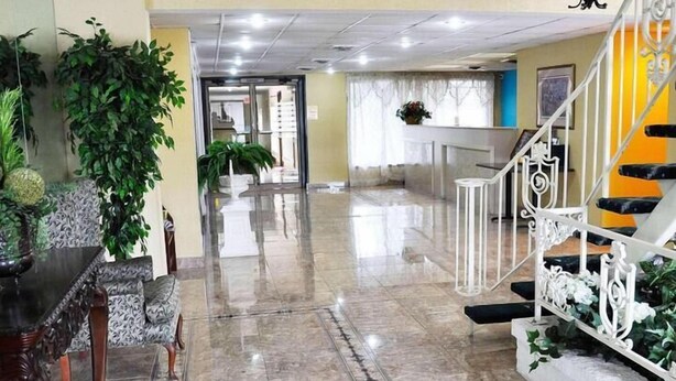 A lobby with a marble floor, a reception desk, a staircase, and potted plants. - Avalon Inn (Sandusky)