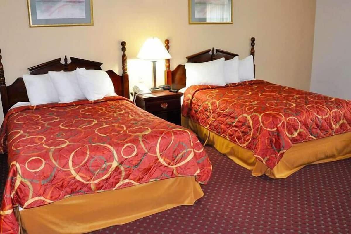 Quarto de hotel com duas camas de casal, cada uma com colcha estampada em vermelho e dourado, uma cabeceira de madeira e uma mesa de cabeceira com abajur.