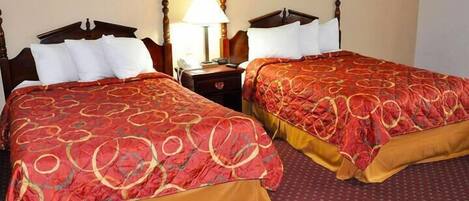 A hotel room with two double beds, each with a red and gold patterned bedspread, a wooden headboard, and a nightstand with a lamp.