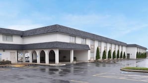 A modern building with a covered entrance, multiple parking spaces, and a landscaped area with trees. - Avalon Inn (Sandusky)