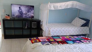 A bedroom with a bed, a TV on a black stand, a quilt, and a canopy bed.