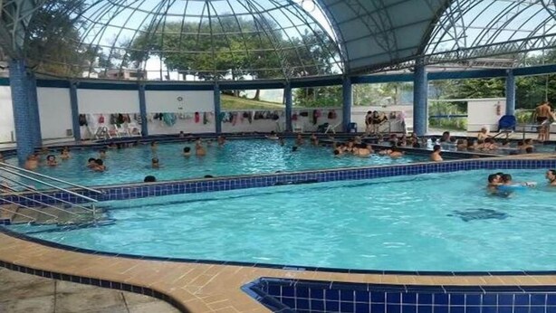 Una piscina techada con múltiples carriles, un área cubierta y un bordeado de baldosas alrededor de la piscina.