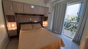 Un dormitorio con cama, armarios de madera, mesitas de noche y un balcón con cortinas.