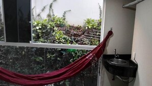 Una ventana con vista a un jardín, una hamaca roja y un lavamanos.