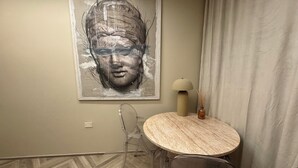 Habitació amb un quadre abstracte gran, una taula rodona amb una làmpada i una cadira.