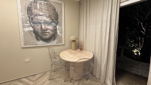 Zona de menjador moderna amb taula rodona, cadires transparents, làmpada i un gran quadre abstracte a la paret.