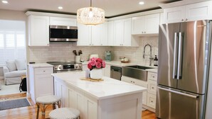 A modern kitchen with white cabinetry, stainless steel appliances, and a central island with stools. - Charming Scarborough Beach, Narragansett 3-bedroom home getaway (Narragansett)