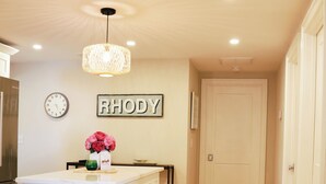 A kitchen with a central island, wooden stools, a pendant light, a clock, and a sign on the wall. - Charming Scarborough Beach, Narragansett 3-bedroom home getaway (Narragansett)