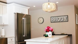 A modern kitchen with white cabinetry, a stainless steel refrigerator, a wooden island with stools, and a hanging light fixture. - Charming Scarborough Beach, Narragansett 3-bedroom home getaway (Narragansett)