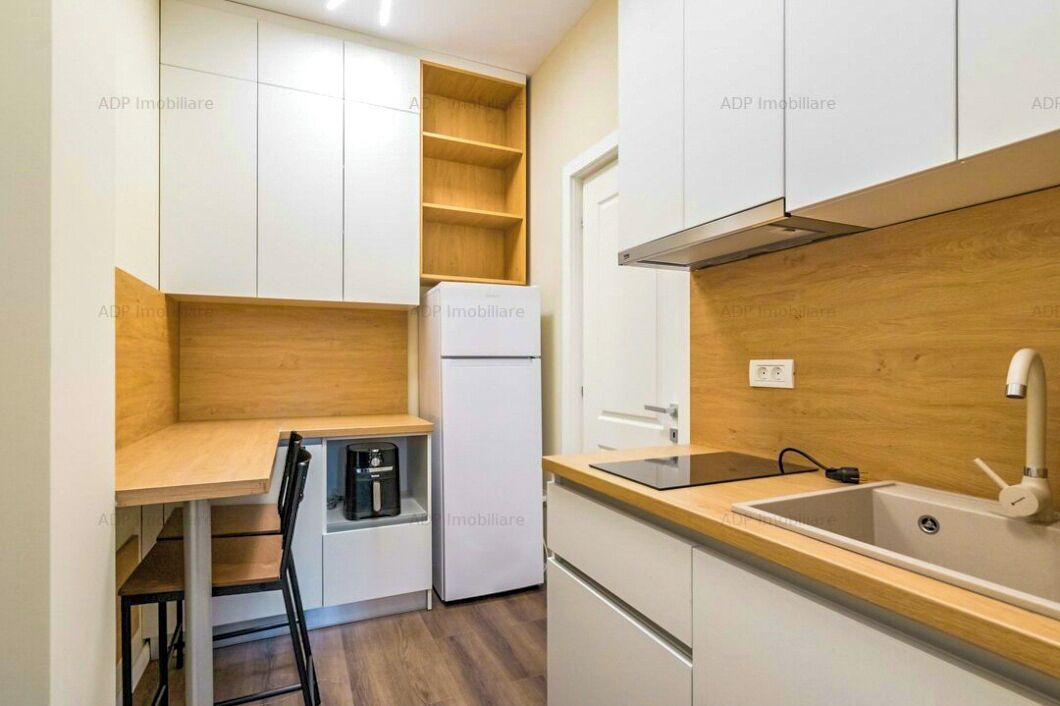 Une cuisine compacte avec des meubles blancs, un four encastré, un réfrigérateur et un plan de travail en bois.