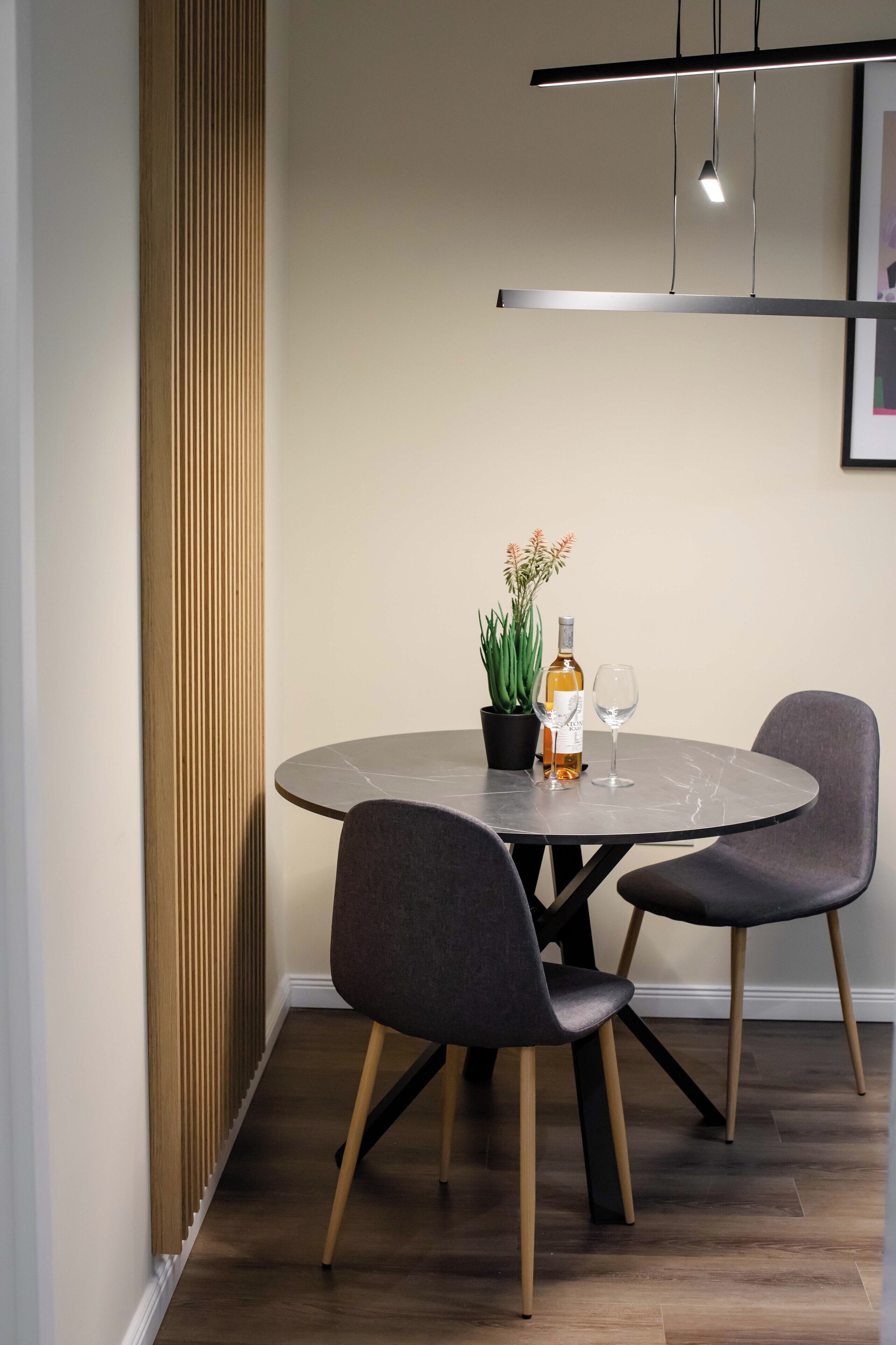 Une table de salle à manger ronde, accompagnée de deux chaises, d’une bouteille de vin et d’une plante en pot.