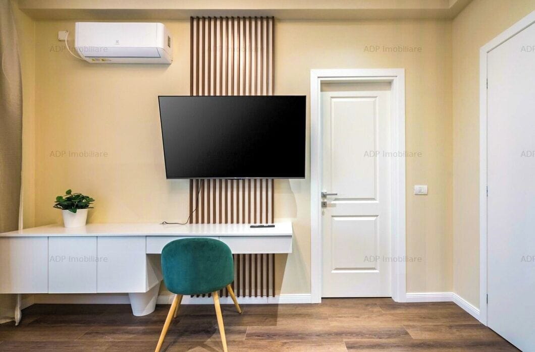 A modern room with a white desk, a black flat-screen TV mounted on the wall, a potted plant, and a green chair.