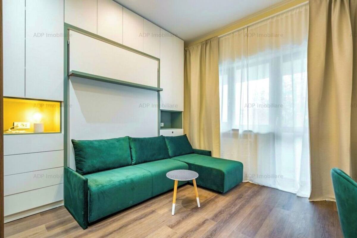 A modern living room with a green sofa, a small round table, and a large window with curtains.