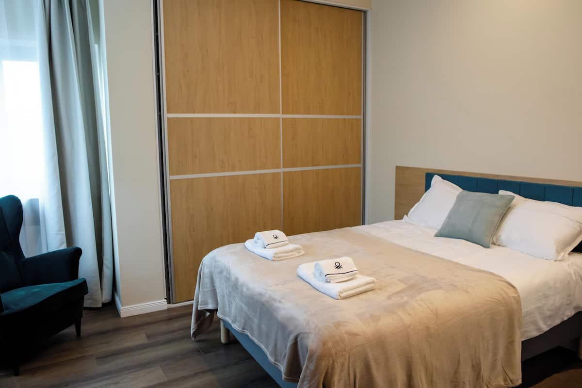 A hotel room with a bed, a chair, and a wooden wardrobe.