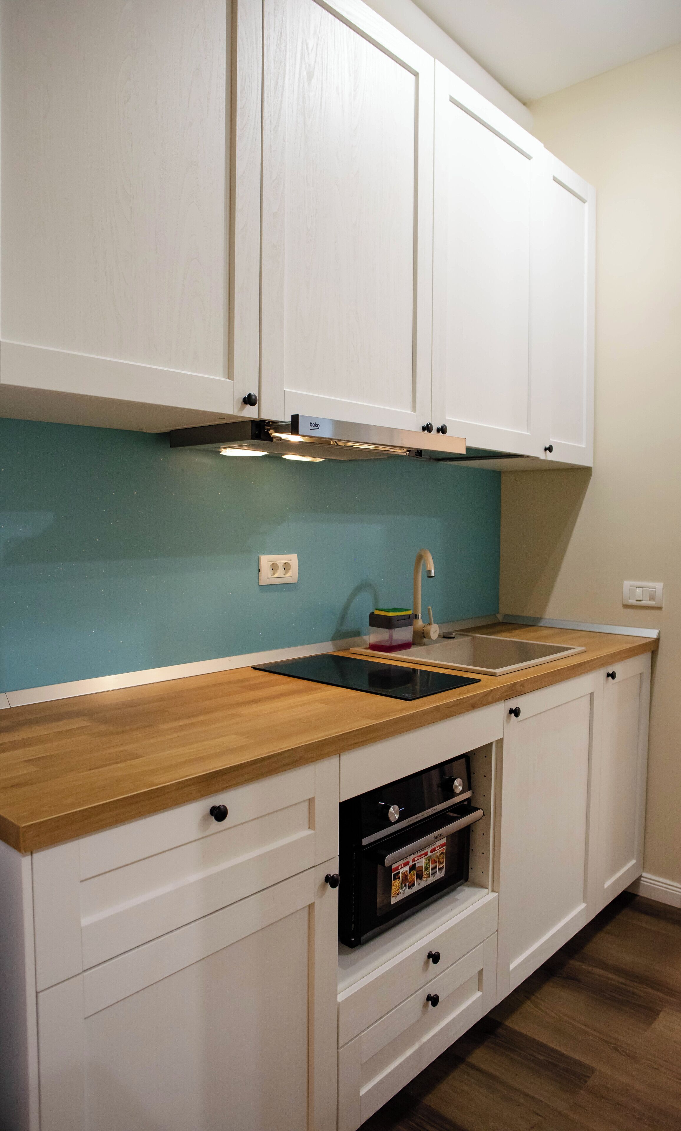 Una cocina con gabinetes blancos, encimera de madera, un lavamanos y un horno.