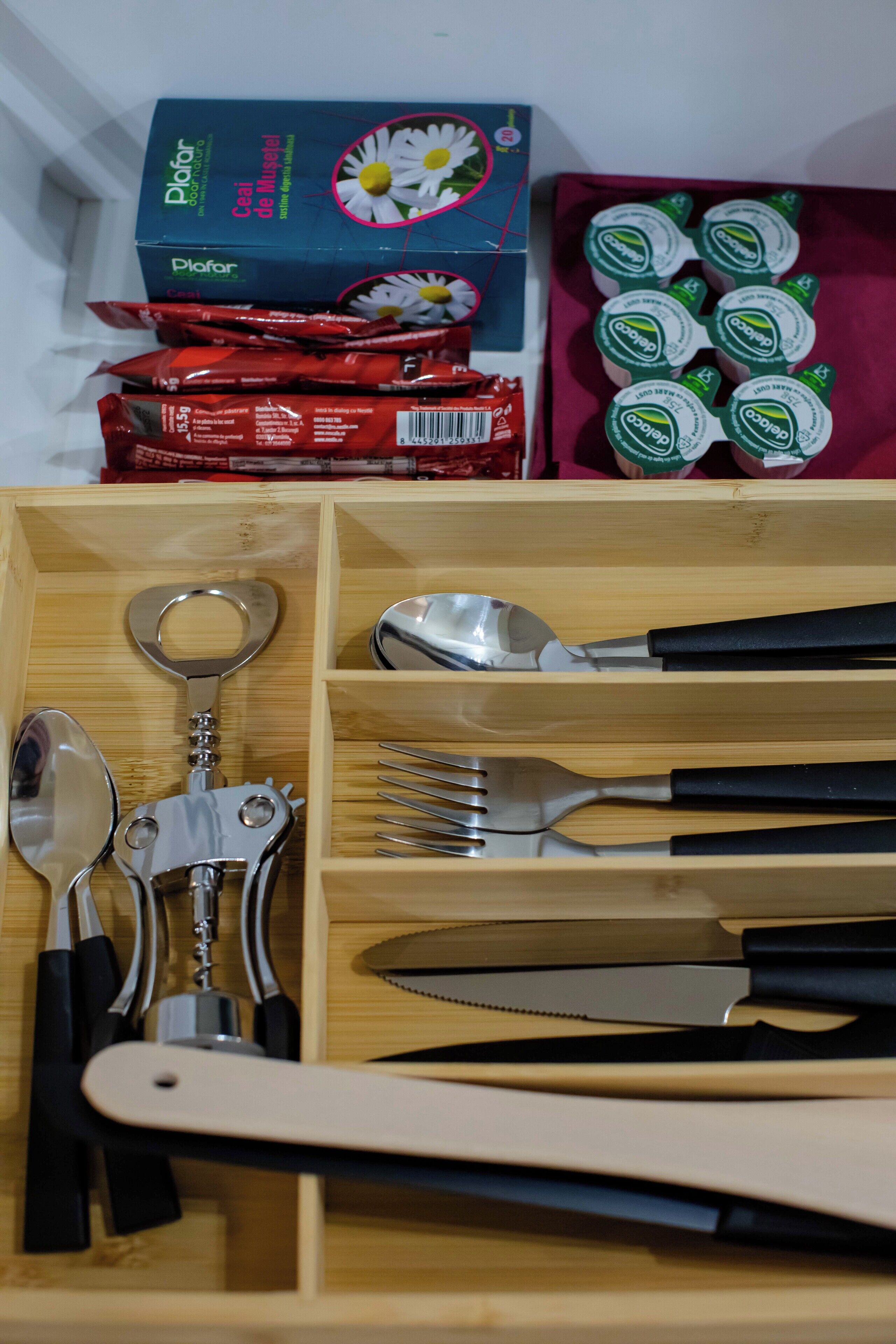 Un tiroir en bois contenant des ustensiles de cuisine, notamment une cuillère, une fourchette, un couteau et un décapsuleur.