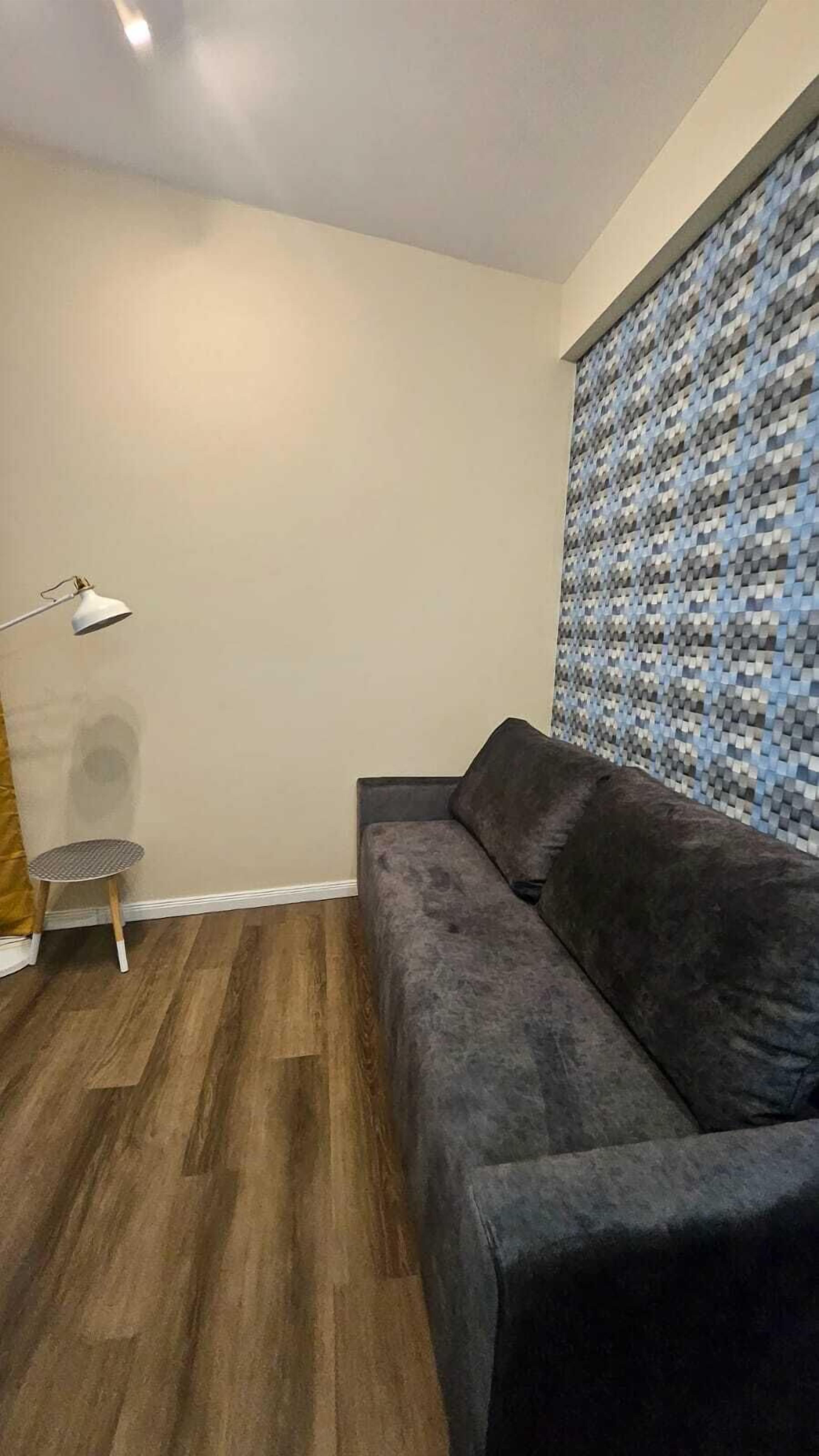 Ein Wohnzimmer mit einem dunkelgrauen Sofa, einem kleinen runden Tisch und einer Lampe.