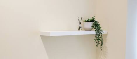 Una habitación de esquina con un escritorio blanco, una silla gris y una estantería con una planta.