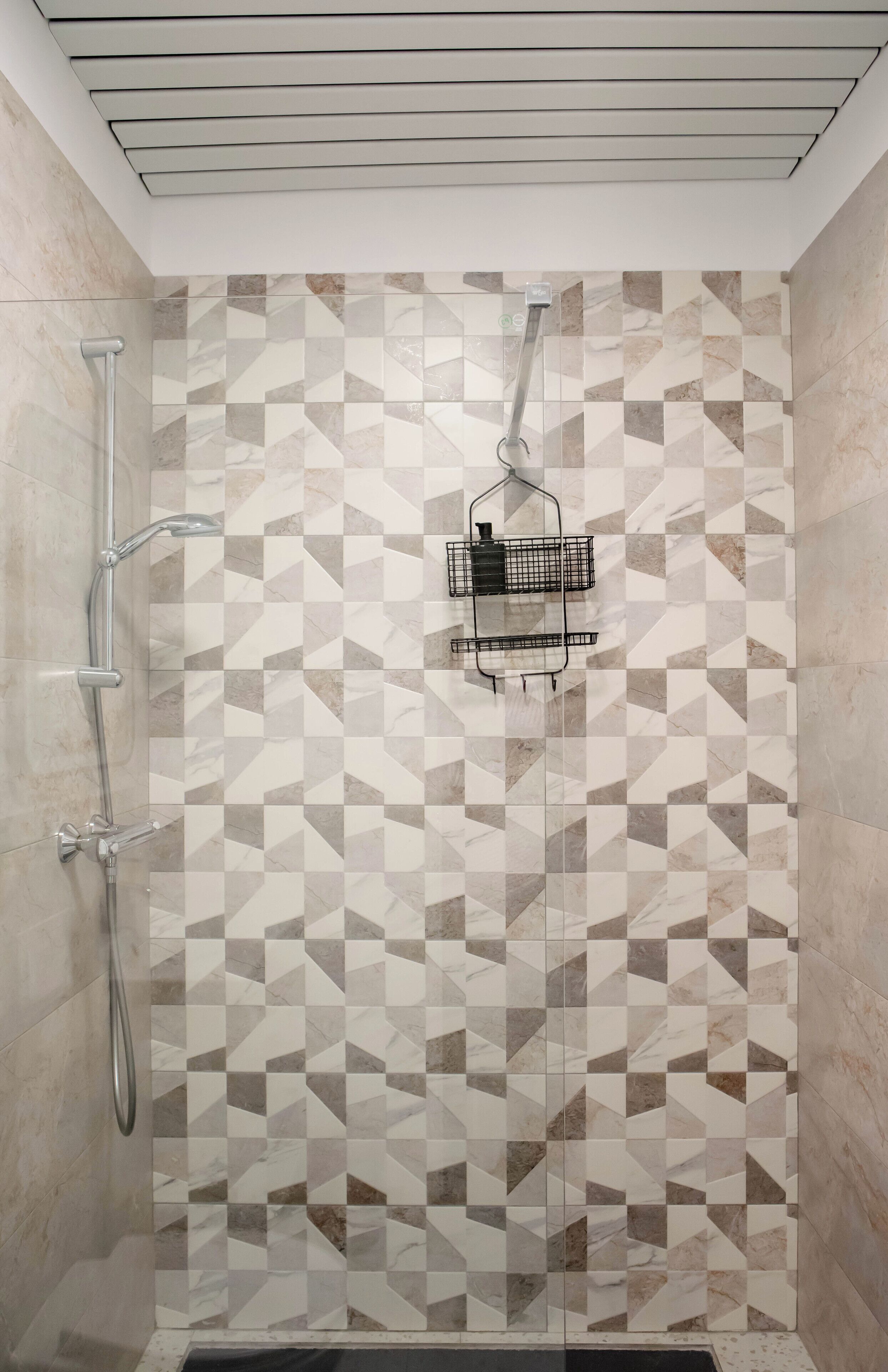 A shower with a geometric tile pattern, a handheld showerhead, and a wall-mounted faucet.
