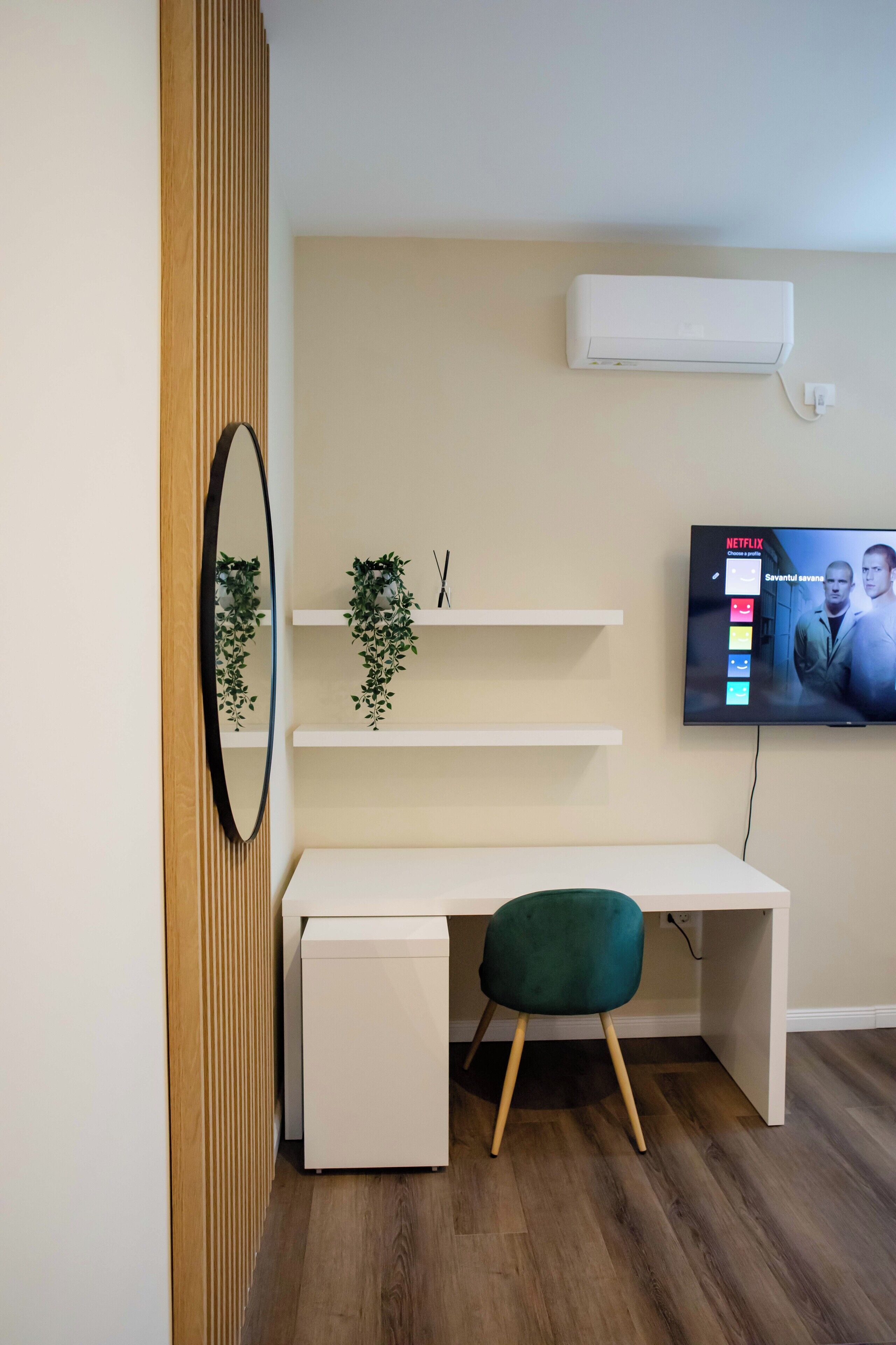 Een moderne kantoorruimte met een wit bureau, een groene stoel, een tv met Netflix en een wandairconditioner.