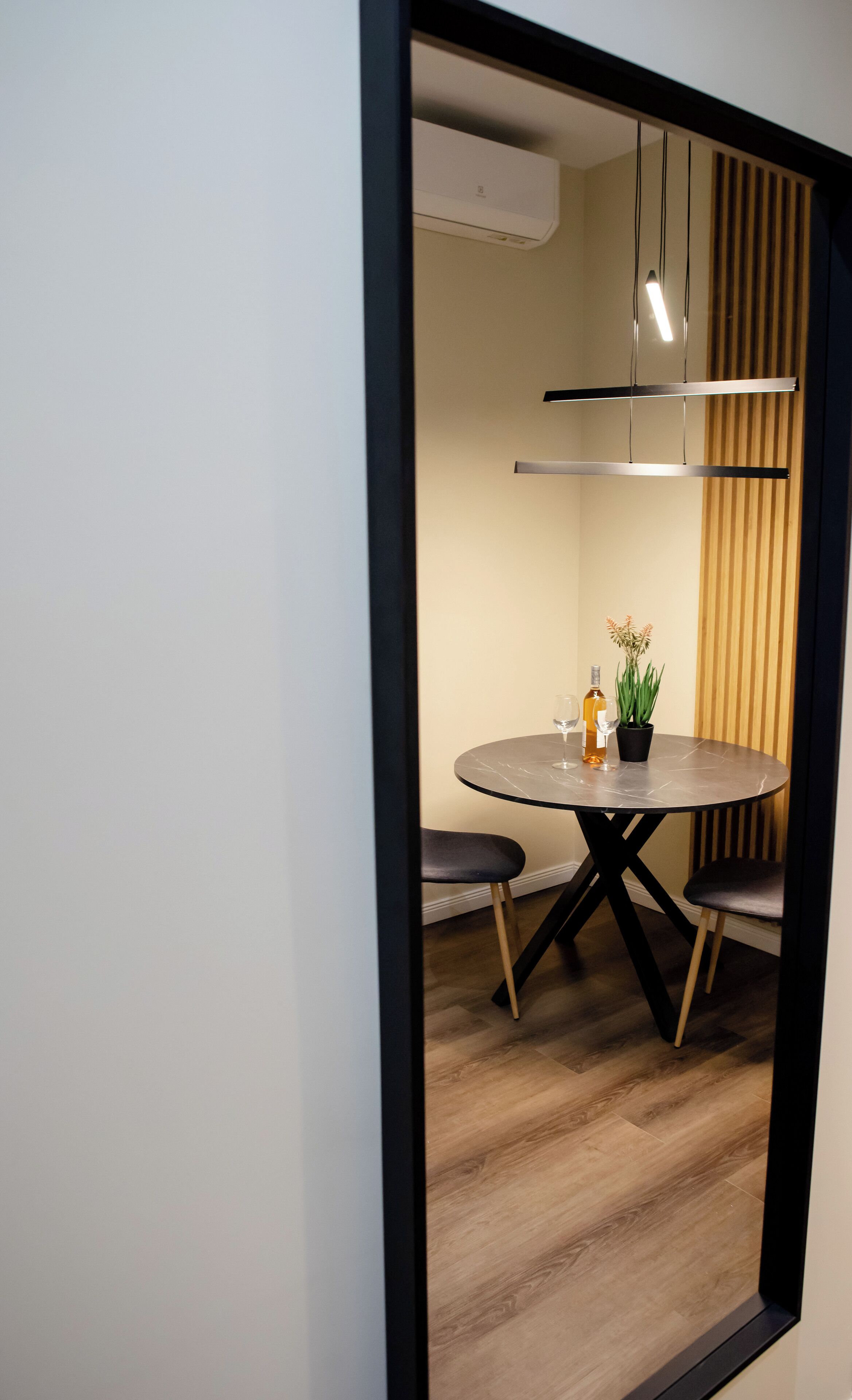 A modern dining area with a round table, two chairs, a potted plant, and a wine bottle.