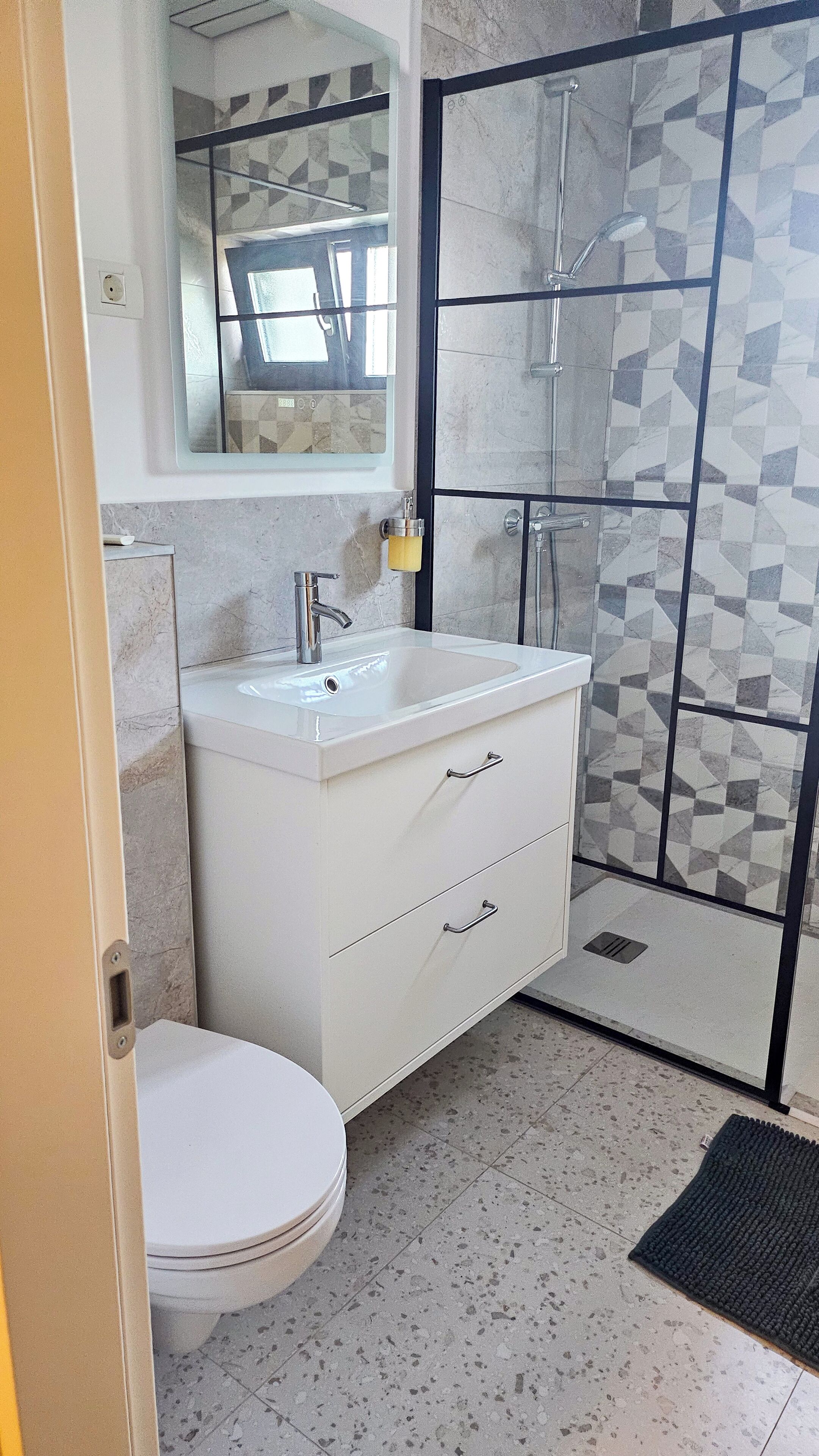 Une salle de bain avec un meuble-lavabo blanc, un évier, des toilettes et un espace douche doté d’une porte en verre.