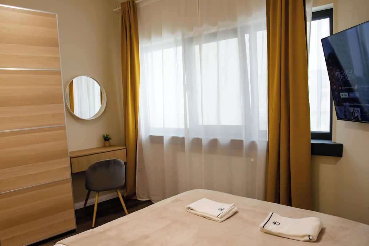 A hotel room with a bed, a desk, a chair, a mirror, and a TV on the wall.