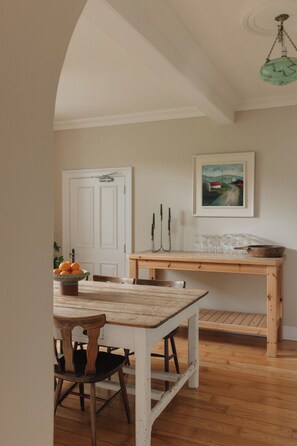 Een rustieke eethoek met een houten tafel en stoelen, een witte deur, en een schilderij aan de muur.