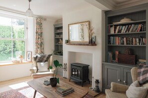 Een gezellige woonkamer met een open haard, boekenkasten, een bank en een bijzettafeltje.