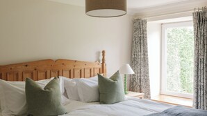 Un dormitorio con cabecera de madera, ropa de cama blanca, almohadas verdes, una lámpara de noche y una ventana con cortinas.