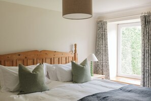 Een slaapkamer met een houten hoofdbord, wit beddengoed, groene kussens, een bedlampje en een raam met gordijnen.