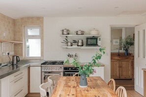 Een keuken met een houten tafel, witte kastjes, een fornuis en een magnetron.