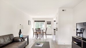 Ein modernes Wohnzimmer mit Ledersofa, Couchtisch mit Zeitschriften, TV-Standfuß und Essbereich mit Stühlen und Tisch.