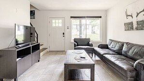 Ein modernes Wohnzimmer mit Flachbildfernseher, einer Ledersofa, einem Couchtisch und einem großen Fenster.