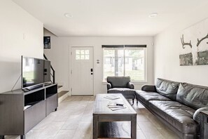 Uma sala de estar moderna com televisão de tela plana, sofá de couro, mesa de centro e uma janela grande.